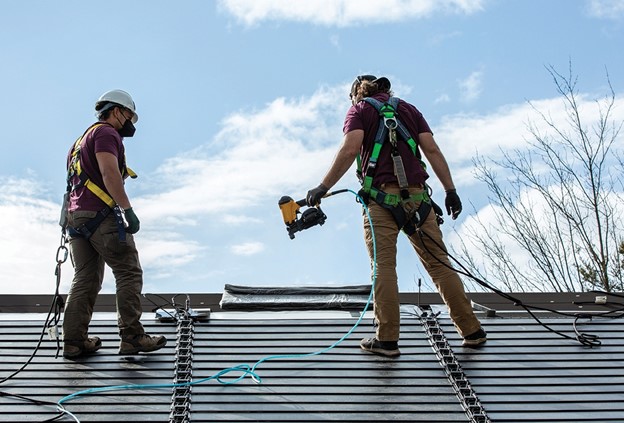 Two roofing contractors installing GAF Solar Shingles on the roof of a house.