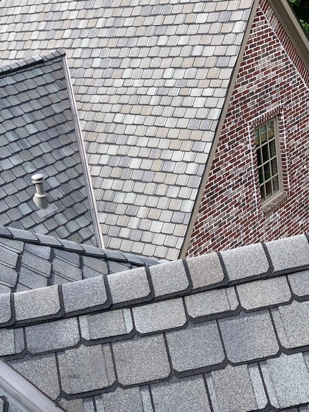 Asphalt shingles on the many facets of a cross-gable roof on a brick house