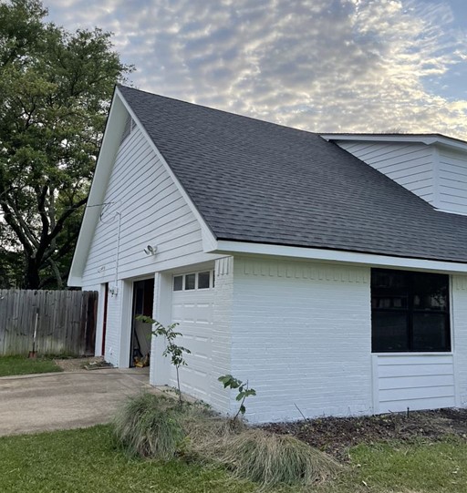 Side view of a recently remodeled home with a brand-new roof. The brick siding of the home has been whitewashed, and the windows have been replaced.