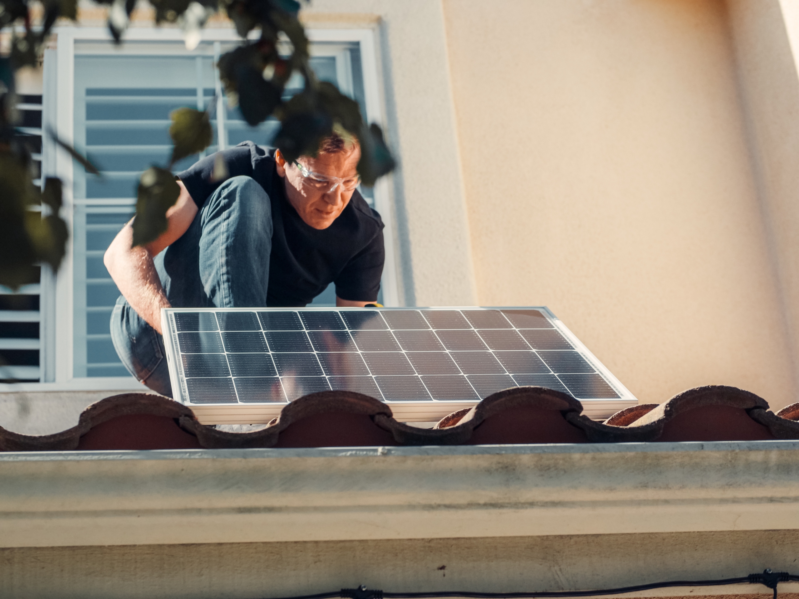 Solar panel maintenance being done on a roof by a man wearing safety glasses