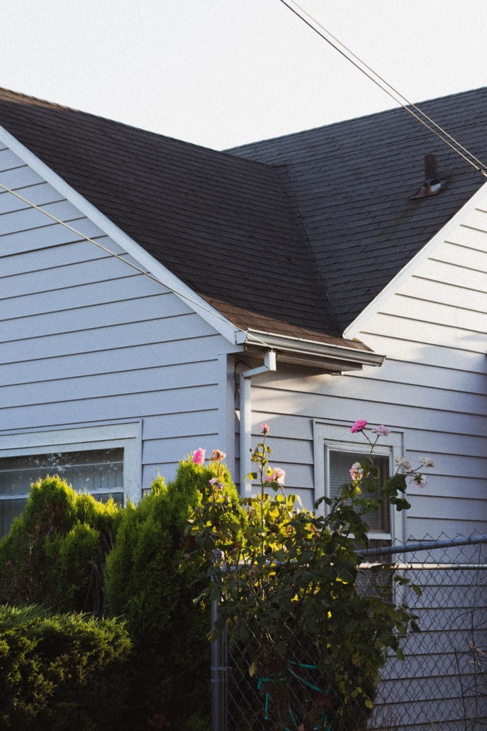 Light gray house after a roof inspection with bushes and flowers growing in front.