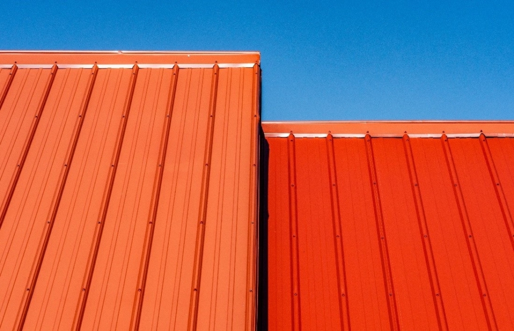 Red, metal roofing against a blue sky, illustrating the cost-saving nature of modern energy-efficient coatings.