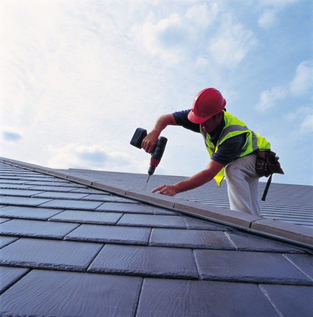 A roofer installs gray slate tiles on a residence. Slate tiles are considered one of the most stylish types of roof shingles by some. They have a premium price tag to match their upscale appearance.