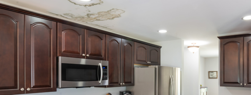 A water-damaged ceiling with water spots staining areas around a light fixture. These water spots are a telltale sign of a roof leak.