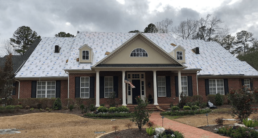 A home with its roof shingles removed during a roof replacement. A replacement on this home’s roof is likely to increase its value, as it’s a larger, older home.